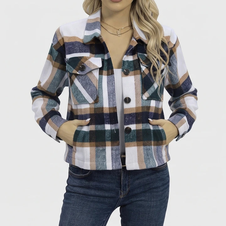 Woman wearing a white, brown, blue, and green plaid jacket with chest pockets, hands in hip pockets, over jeans.