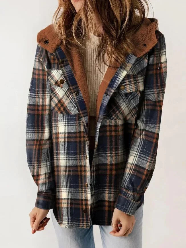 Woman wearing a plaid hooded jacket in shades of navy, brown, and cream over a ribbed cream sweater.