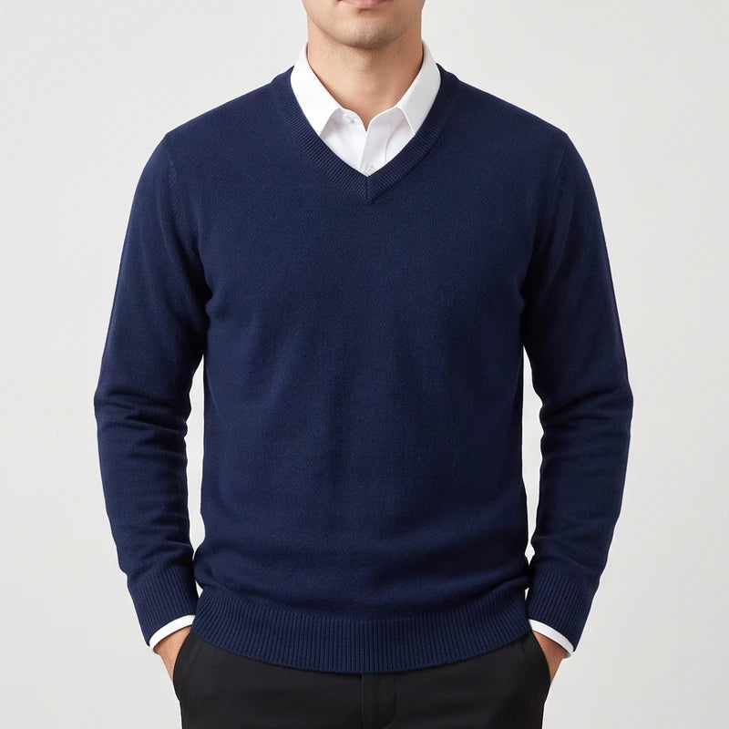 Man wearing a navy blue knit v-neck sweater layered over a white collared shirt against a white background.