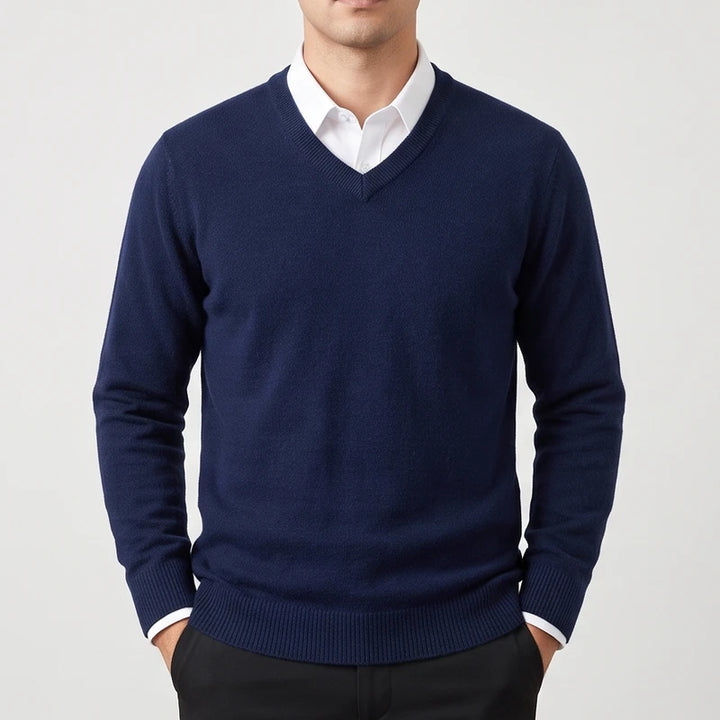 Man wearing a navy blue knit v-neck sweater layered over a white collared shirt against a white background.
