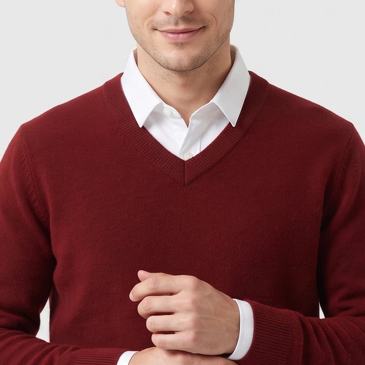 Man wearing a burgundy V-neck knit sweater layered over a white collared shirt against a plain light background.