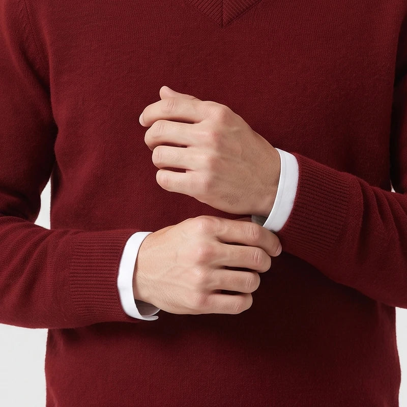 Man wearing a burgundy V-neck wool sweater layered over a white shirt while adjusting his ribbed sleeve cuffs.