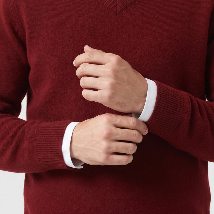 Man wearing a burgundy V-neck wool sweater layered over a white shirt while adjusting his ribbed sleeve cuffs.