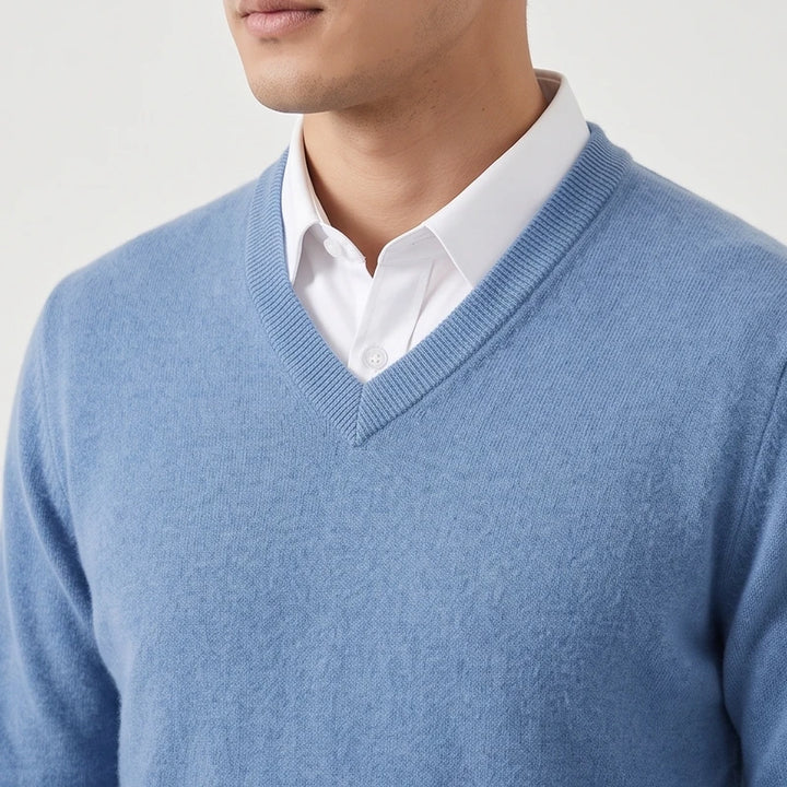 Close-up of a man wearing a light blue knit v-neck sweater layered over a white collared dress shirt.