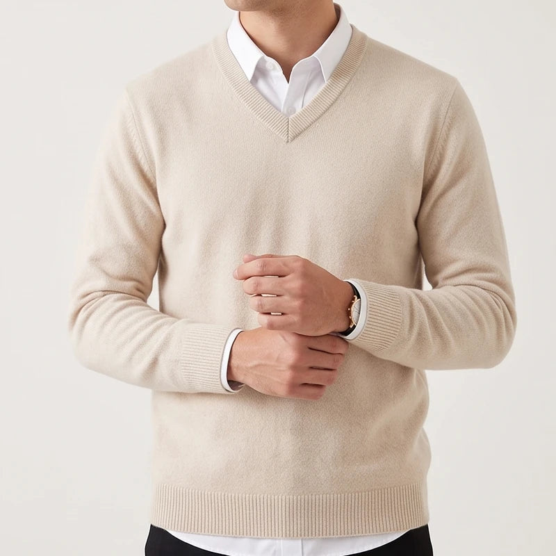Man wearing a light beige v-neck wool sweater layered over a white dress shirt, adjusting his cuff.