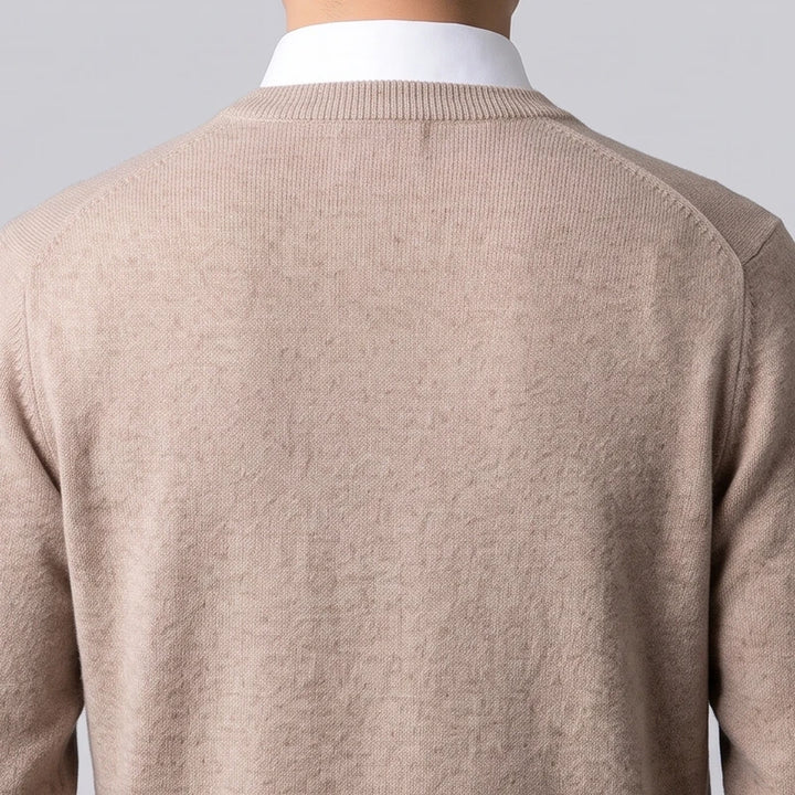 Man wearing a beige fine-knit wool sweater layered over a white collared shirt, seen from behind against a neutral background.