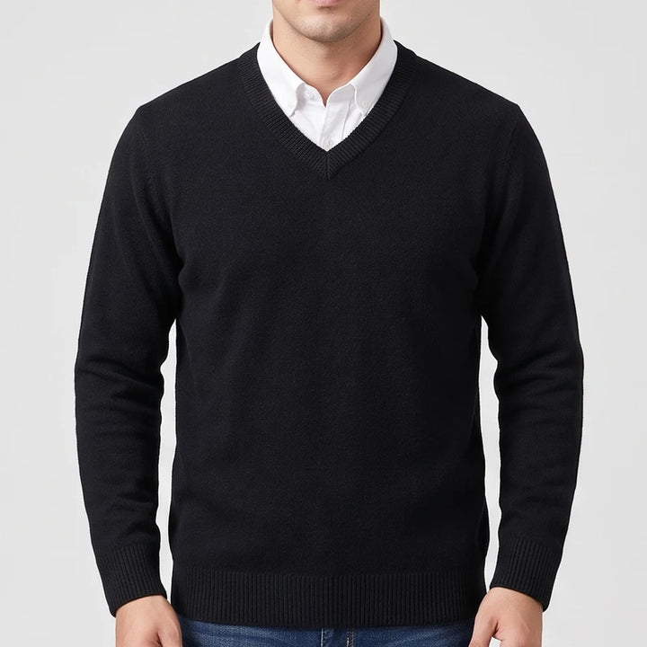 Man wearing a black knit V-neck wool sweater layered over a white collared shirt against a light gray background.