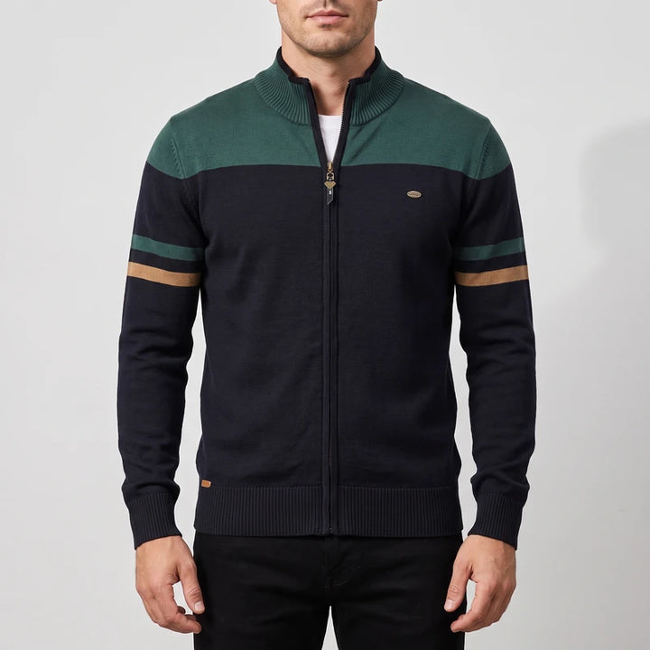 Man wearing a dark blue zip-up sweater with a dark green top block and two green and tan stripes on the left sleeve.